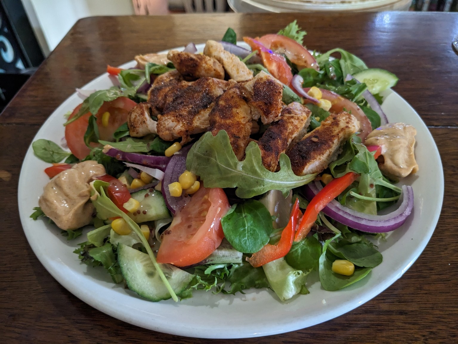 Cajun spiced chicken on a mixed salad with tomato, cucumber and corn
